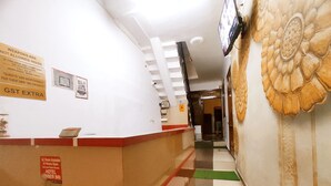 A hotel reception area with a counter, a sign indicating a 24-hour AC room, and a wall with a floral design. - Premium Rooms For Corporates, Couples, Families, Students And Travelers (Ludhiana)