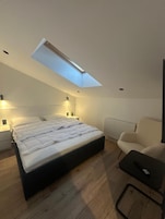 A modern bedroom with a skylight, a bed, bedside lamps, a radiator, and a chair.