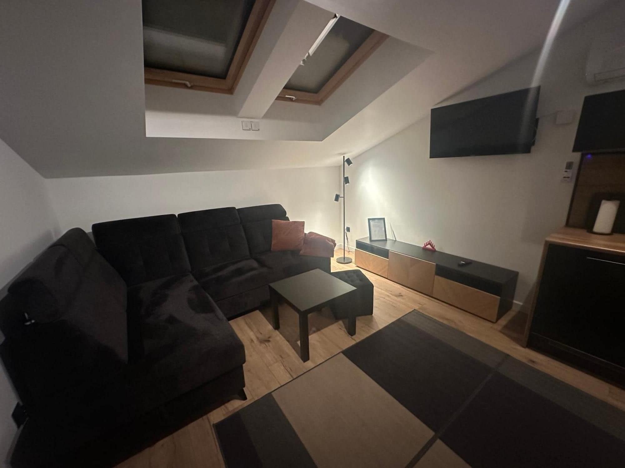 A modern living room with a sectional sofa, a small table, a floor lamp, and a TV mounted on the wall.