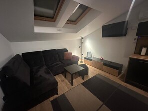 A modern living room with a sectional sofa, a small table, a floor lamp, and a TV mounted on the wall. - Mała Gardenia (Nowy Targ)