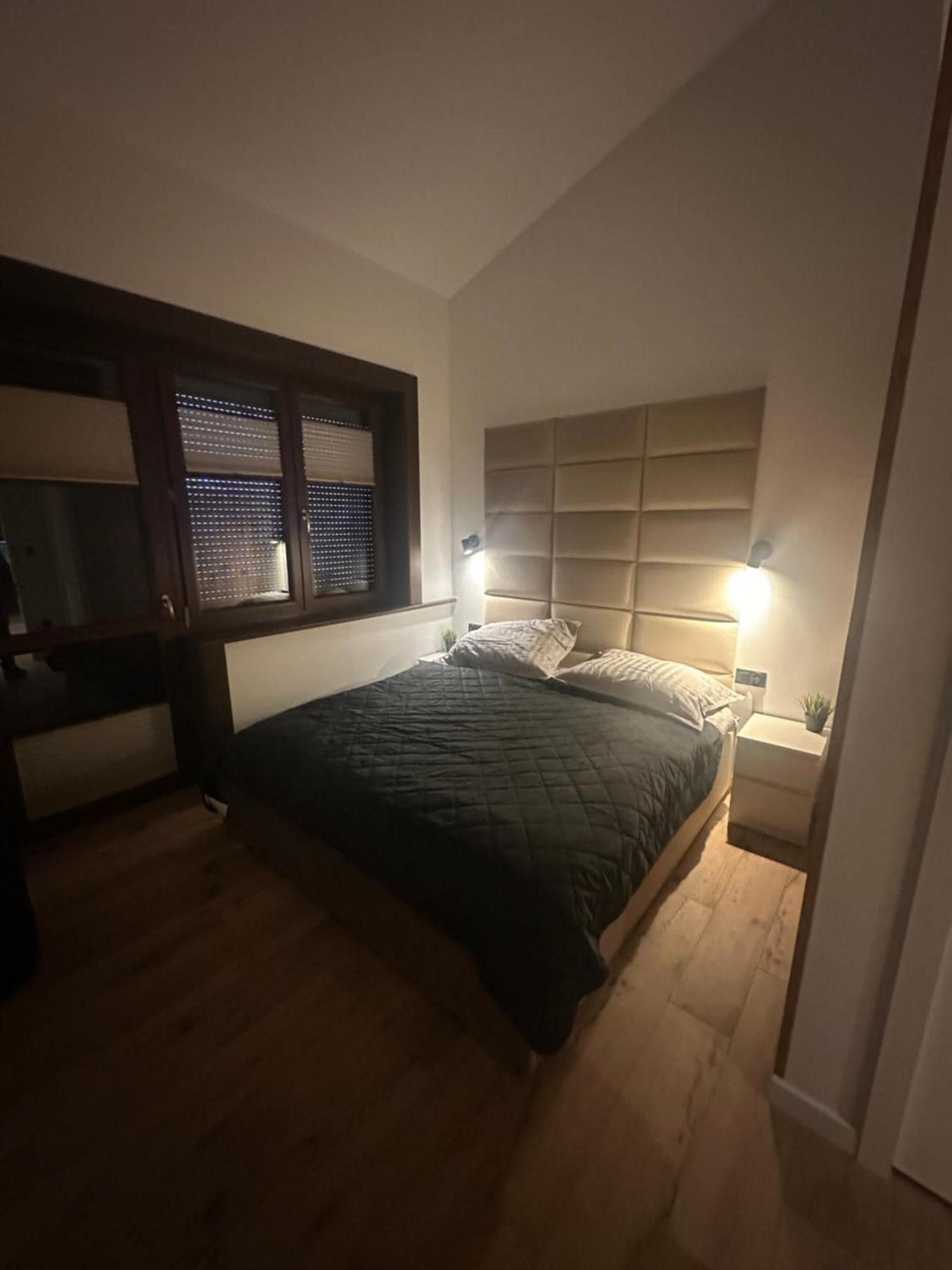 A bedroom with a bed, a nightstand, a lamp, and a window with blinds.