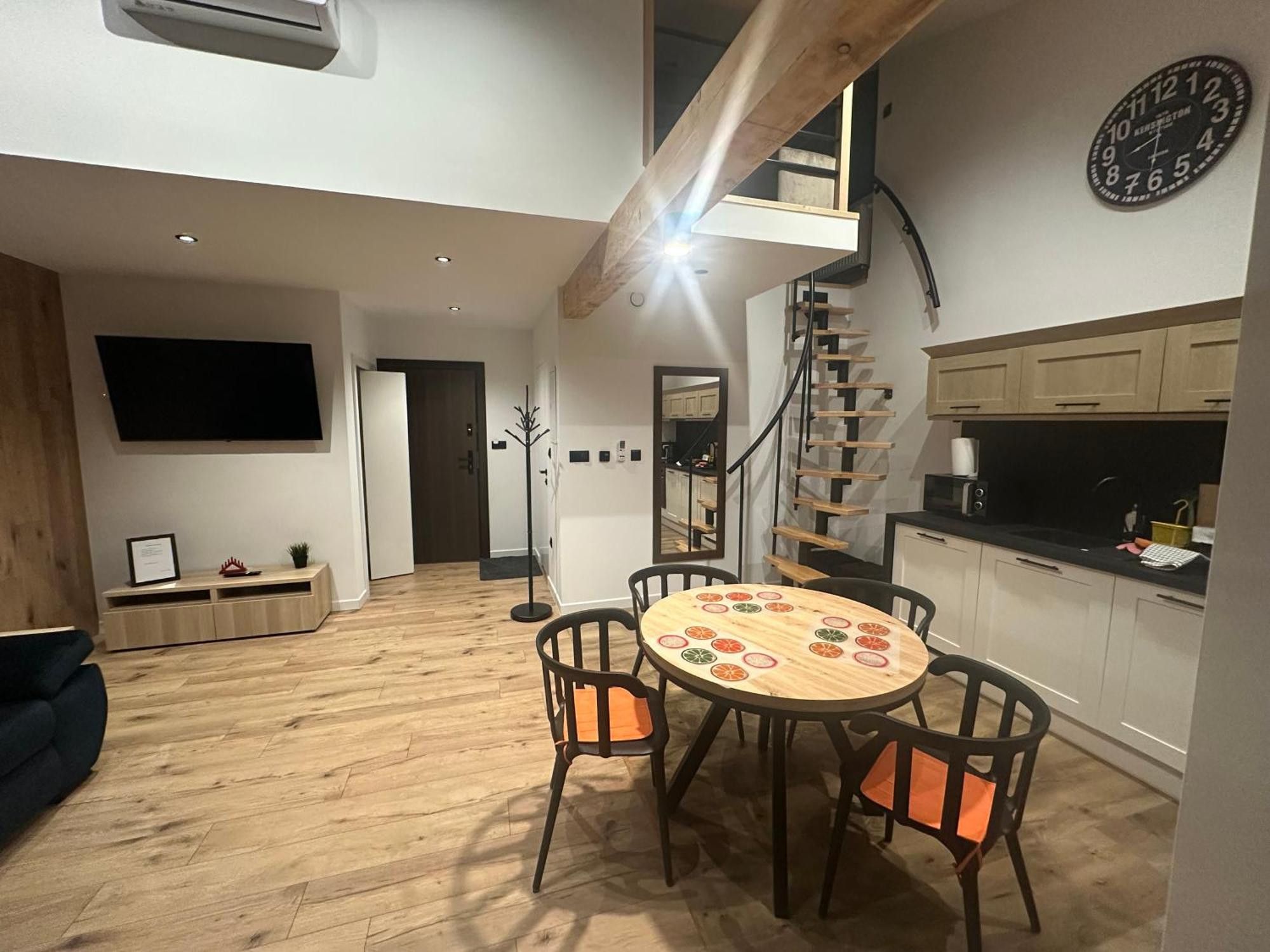 Una cocina moderna con una escalera de madera, un comedor con una mesa redonda y un televisor de pantalla plana montado en la pared.