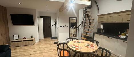 A modern kitchen with a wooden staircase, a dining area with a round table, and a flat-screen TV mounted on the wall.