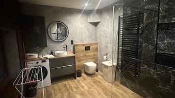 Un baño moderno con piso de madera, un espejo redondo, un lavabo, un inodoro y una zona de ducha con puerta de vidrio.