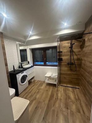 Un baño pequeño con lavadora, lavamanos y zona de ducha.