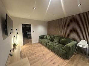 Una sala de estar moderna con un sofá verde, suelo de madera y un televisor montado en la pared.