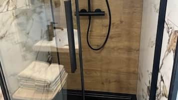 Zona de ducha con mampara de vidrio, pared de madera y un perchero.