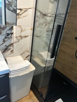 A bathroom with a glass shower enclosure, a marble wall, and a towel rack with folded towels. - Mała Gardenia (Nowy Targ)