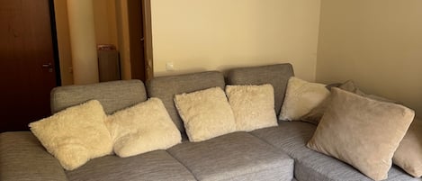 A living room with a grey sofa, beige and brown cushions, a white coffee table, and a wall clock.