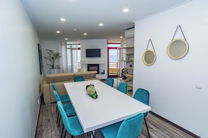 A modern living room with a white dining table, teal chairs, a beige sofa, and a TV mounted on the wall. - ATLANTIC SUN HOUSE - THE INSPIRATION FOR THE GIANT WAVES OF NAZARÉ!!! (Nazaré)