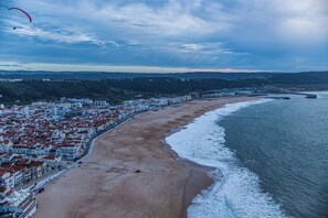 A coastal cityscape with a beach, buildings, and a body of water. - ATLANTIC SUN HOUSE - THE INSPIRATION FOR THE GIANT WAVES OF NAZARÉ!!! (Nazaré)