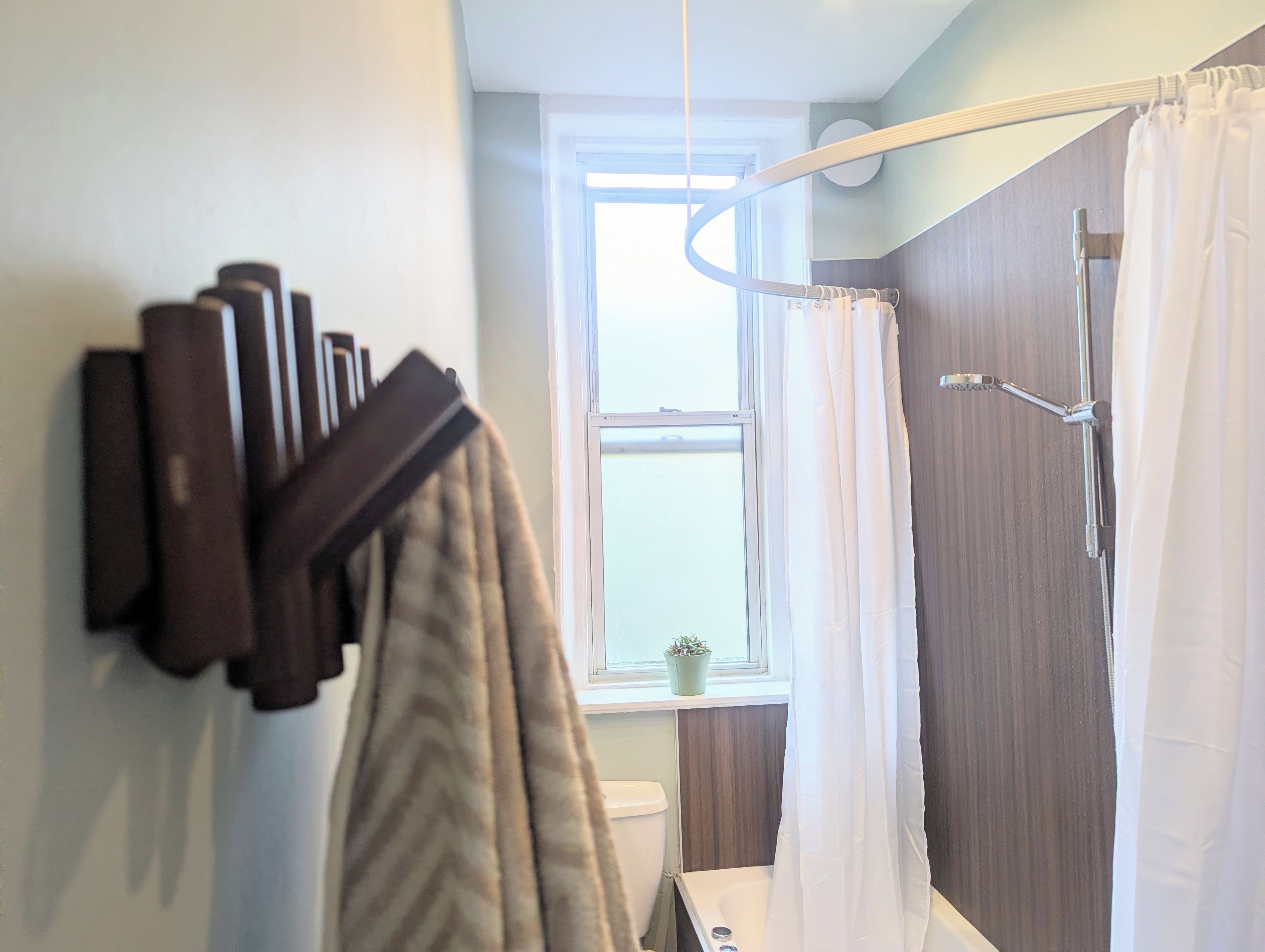A bathroom with a shower curtain, a towel rack, and a window.