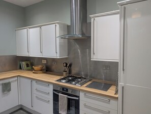 A modern kitchen with white cabinets, a stainless steel range hood, a gas stove, and a built-in oven. - Lovely Victorian Flat in Edinburgh's Historic New Town  (Edinburgh)