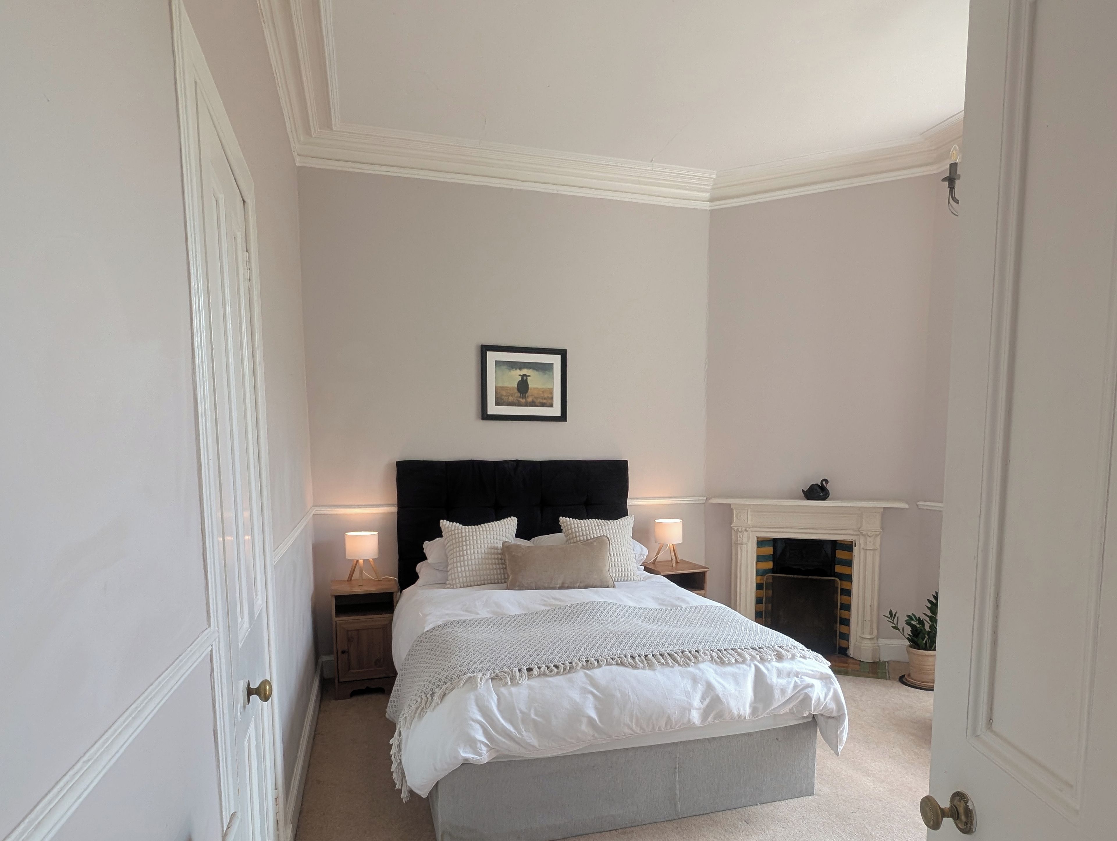 Une chambre à coucher avec un lit, des tables de chevet, une cheminée et un tableau encadré au mur.
