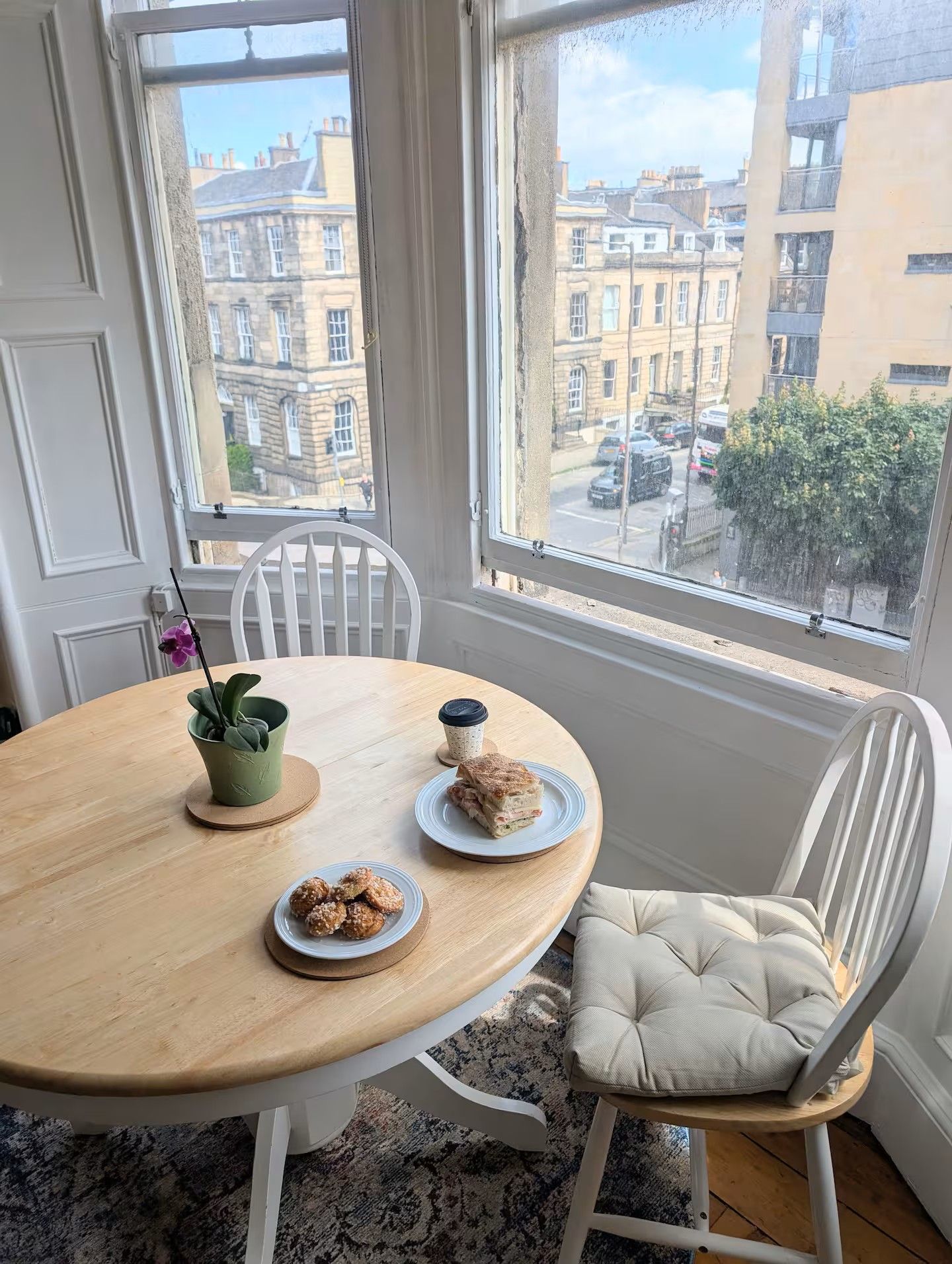 A dining table with plates of food, a chair with a cushioned seat, and a window with a view of buildings.