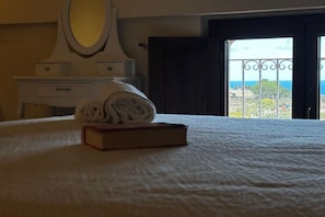 A hotel room with a bed, a rolled towel, a book, a dresser, a mirror, and a view of the sea through an open door. - Capovillas - Silent Country House (Gasponi)