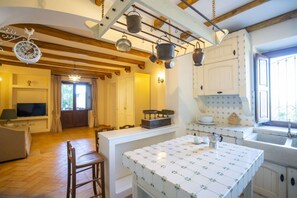 A kitchen with a tiled backsplash, wooden beams, hanging pots, and a television in the living area. - Capovillas - Silent Country House (Gasponi)