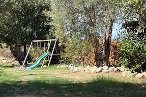 A playground with a slide and swing set, surrounded by trees and a stone wall. - Capovillas - Silent Country House (Gasponi)