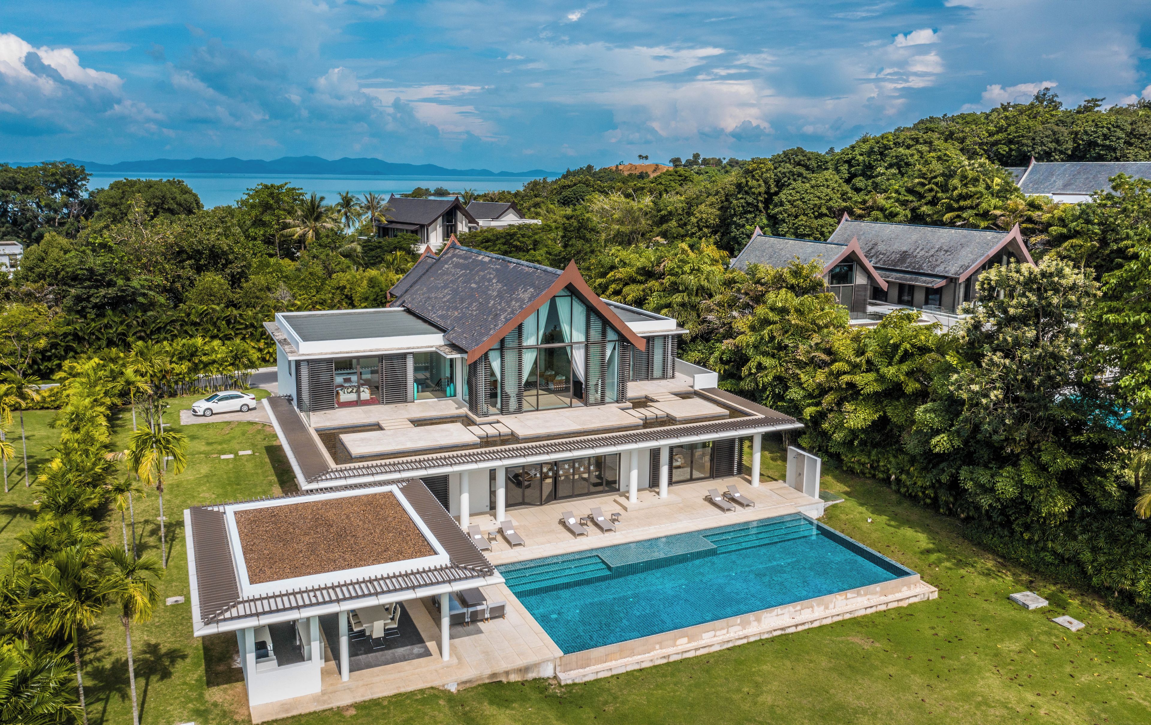 A modern house with a large swimming pool, surrounded by lush greenery and a view of the sea.