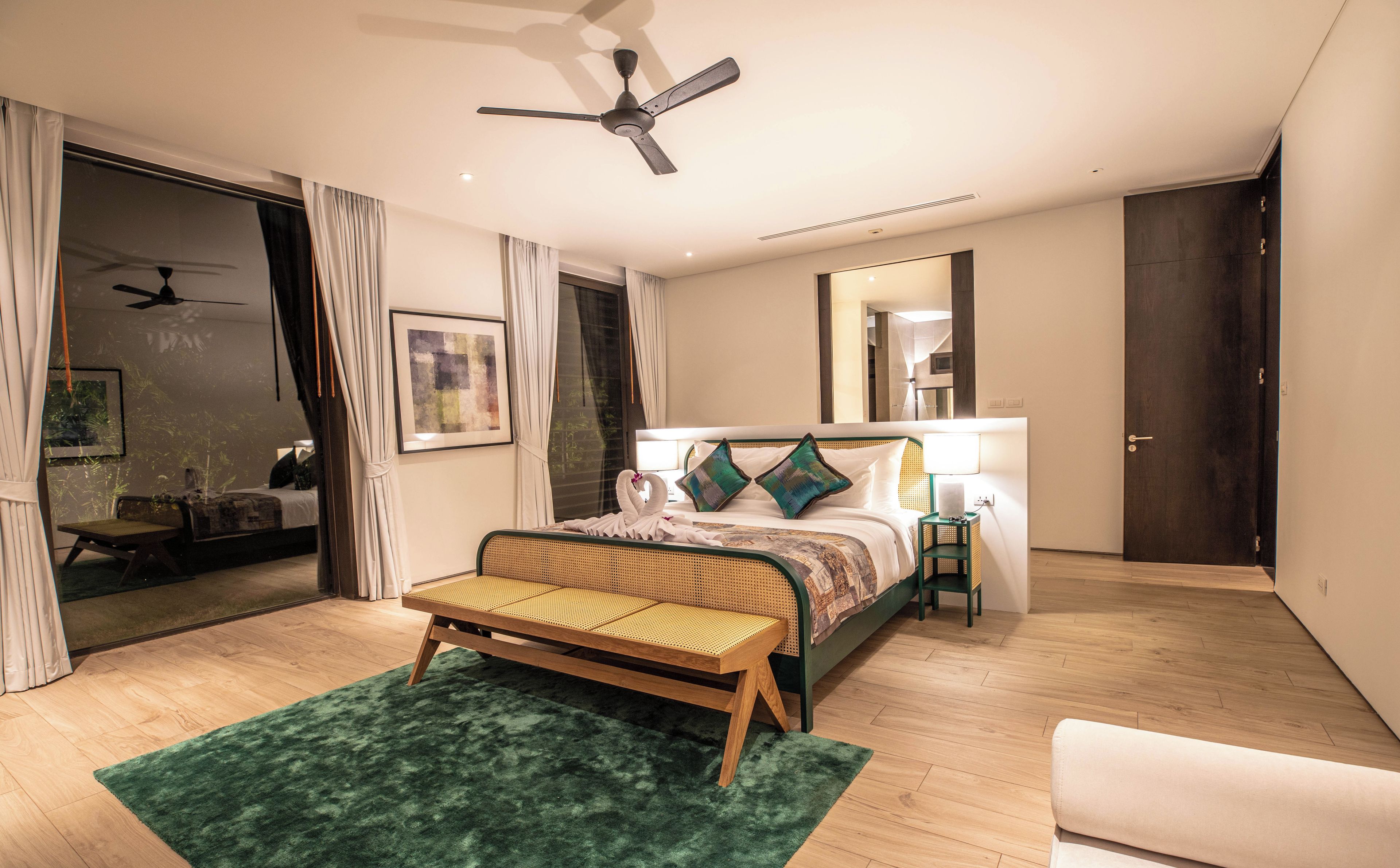Un dormitorio moderno con cama, banca, ventilador de techo, mesita de noche y espejo.