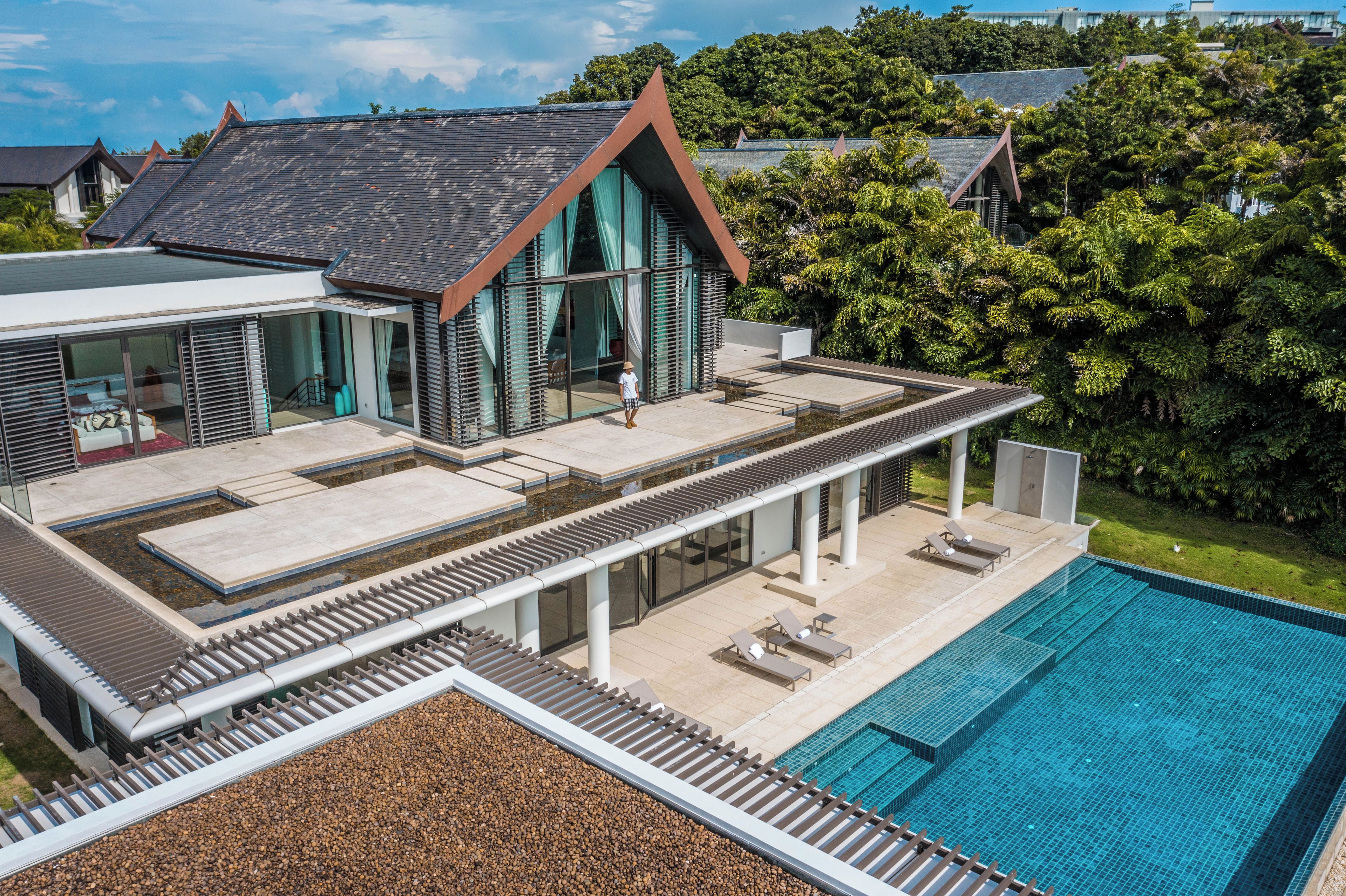 Une maison moderne dotée d’une piscine, d’un patio couvert et offrant une vue sur la verdure environnante.