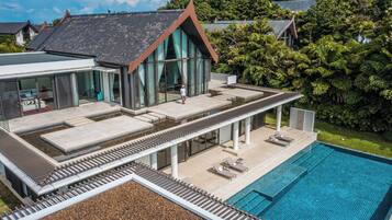 Une maison moderne dotée d’une piscine, d’un patio couvert et offrant une vue sur la verdure environnante.