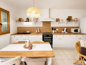 Una cocina moderna con armarios blancos, encimera de madera, una mesa de comedor con mantel blanco y una silla de mimbre.