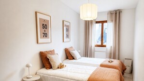 Een slaapkamer met twee bedden, een nachtkastje, een lamp, een vloerkleed en een wieg.