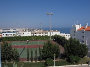 A tennis court surrounded by trees and buildings with a view of the sea. - Spacious 2 bed 2 bath apartment in beautiful Windmill Hill complex with Air Con. (Albufeira)