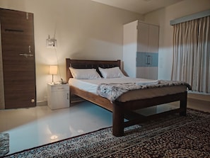 A bedroom with a bed, bedside table, lamp, wardrobe, and a patterned rug. - Bliss Paradise Resort  (Malvan)