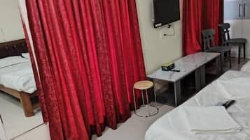 A hotel room with two beds, a desk, a chair, a TV, and red curtains.