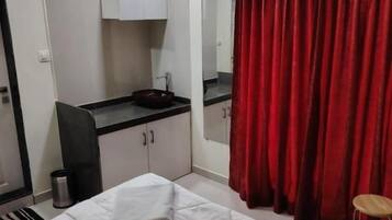 A hotel room with a bed, a desk with a sink, a mirror, and a red curtain.