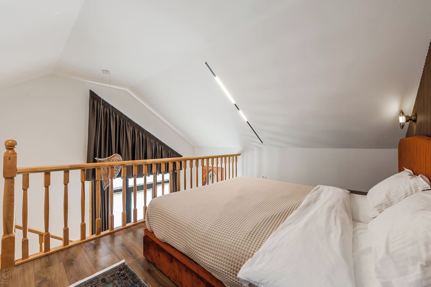 Une chambre avec un plafond en pente, un escalier en bois, un lit avec une literie blanche et une table de chevet.