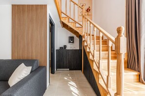 Un salon moderne avec un canapé gris, un mur lambrissé en bois et un escalier avec des rampes en bois.
