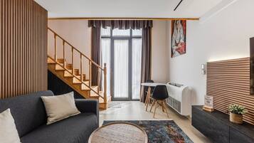 Un salon moderne comprenant un canapé, une table basse, un coin repas avec des chaises, un escalier et une grande fenêtre avec des rideaux.
