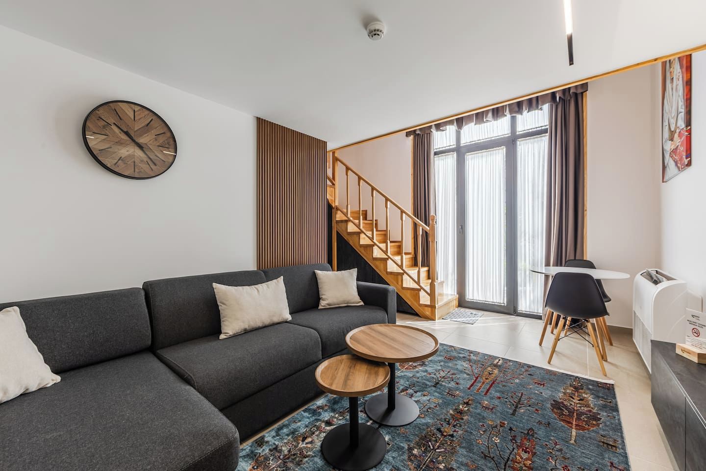 Un salon moderne avec un canapé gris, une table basse ronde en bois et un escalier menant à l’étage supérieur.