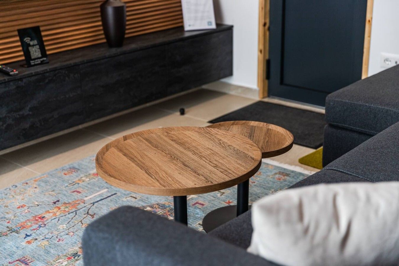 Un salon moderne avec un canapé, deux petites tables d’appoint rondes en bois, une console sombre et un tapis à motifs.