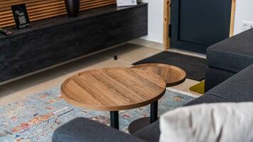 Una sala de estar moderna con un sofá, dos mesitas redondas de madera, un mueble consola oscuro y una alfombra estampada.