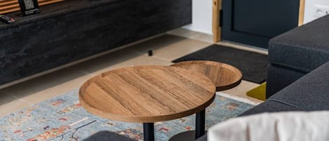 A modern living room with a sofa, two round wooden side tables, a dark console table, and a patterned rug.