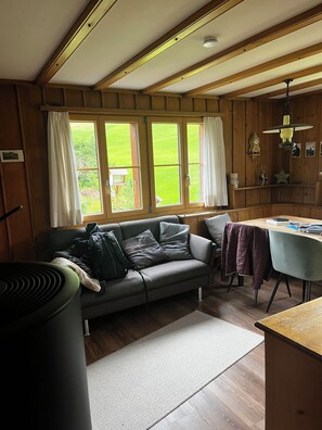 A cozy cabin interior with a sofa, a table, and a window overlooking a green landscape. - Buebebärg Ferienhaus, Dusche und Bad, WC, 2 Schlafräume 3.5-Zimmerwohnung by Interhome (Adelboden)