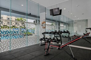 A modern gym with glass walls, exercise equipment, and a television. - Galini by Kozystay - Tebet (South Jakarta)