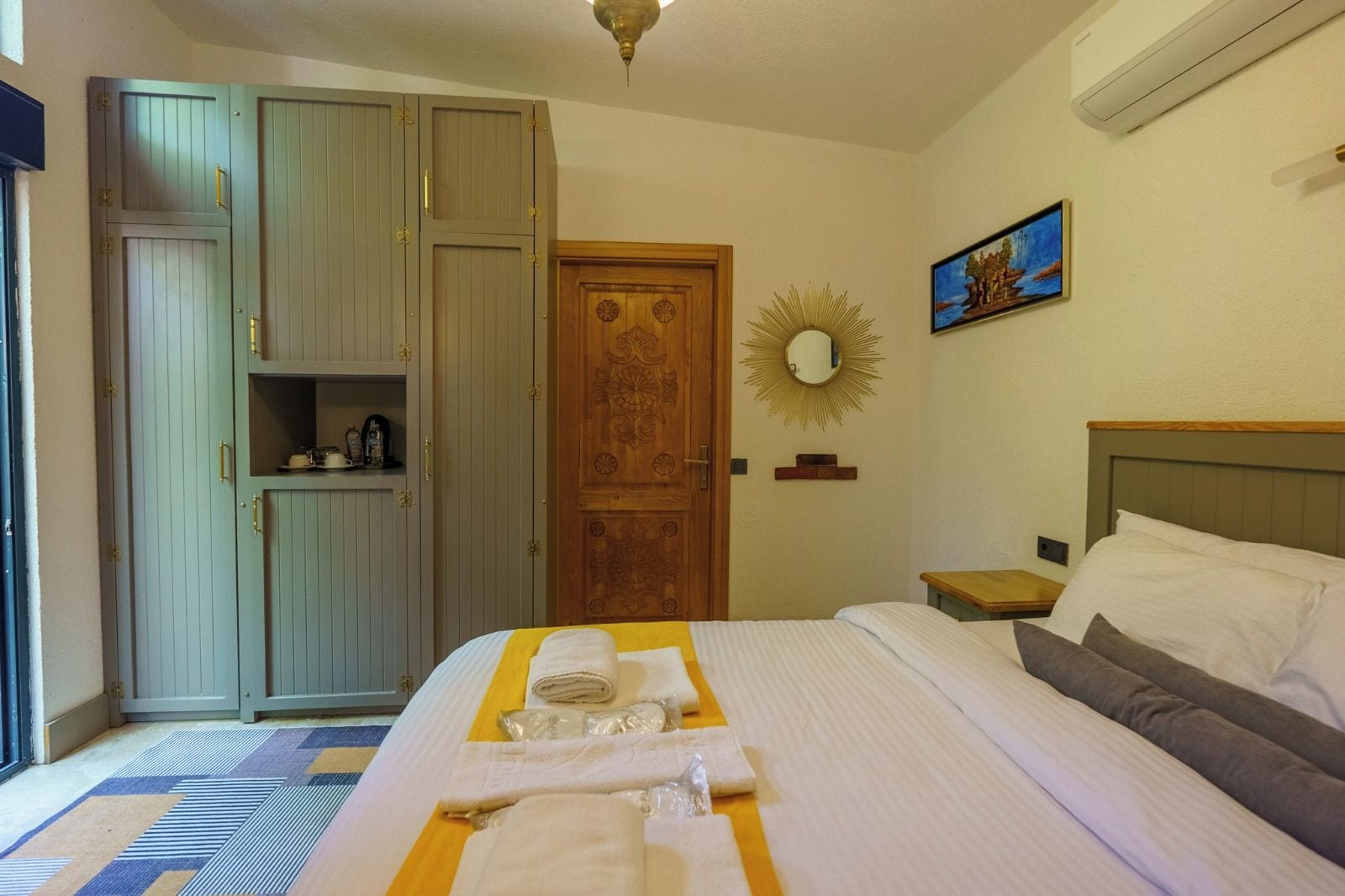 Una habitación de hotel con una cama, un armario, un espejo y un cuadro en la pared.