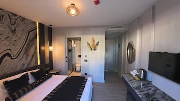 A modern hotel room with a large bed, a TV, a desk, and a bathroom visible through an open door.