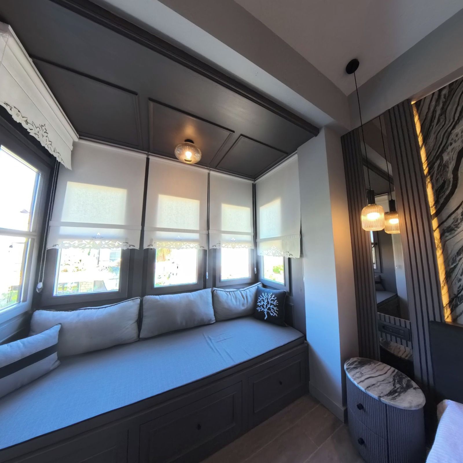A modern room with a built-in bench seating area, large windows with curtains, and a marble-patterned wall.
