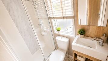 A modern bathroom with a glass shower enclosure, a toilet, a sink with a mirror, and a window with blinds.