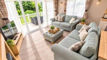 A spacious living room with a grey sofa set, a coffee table, and a TV on a wooden cabinet.