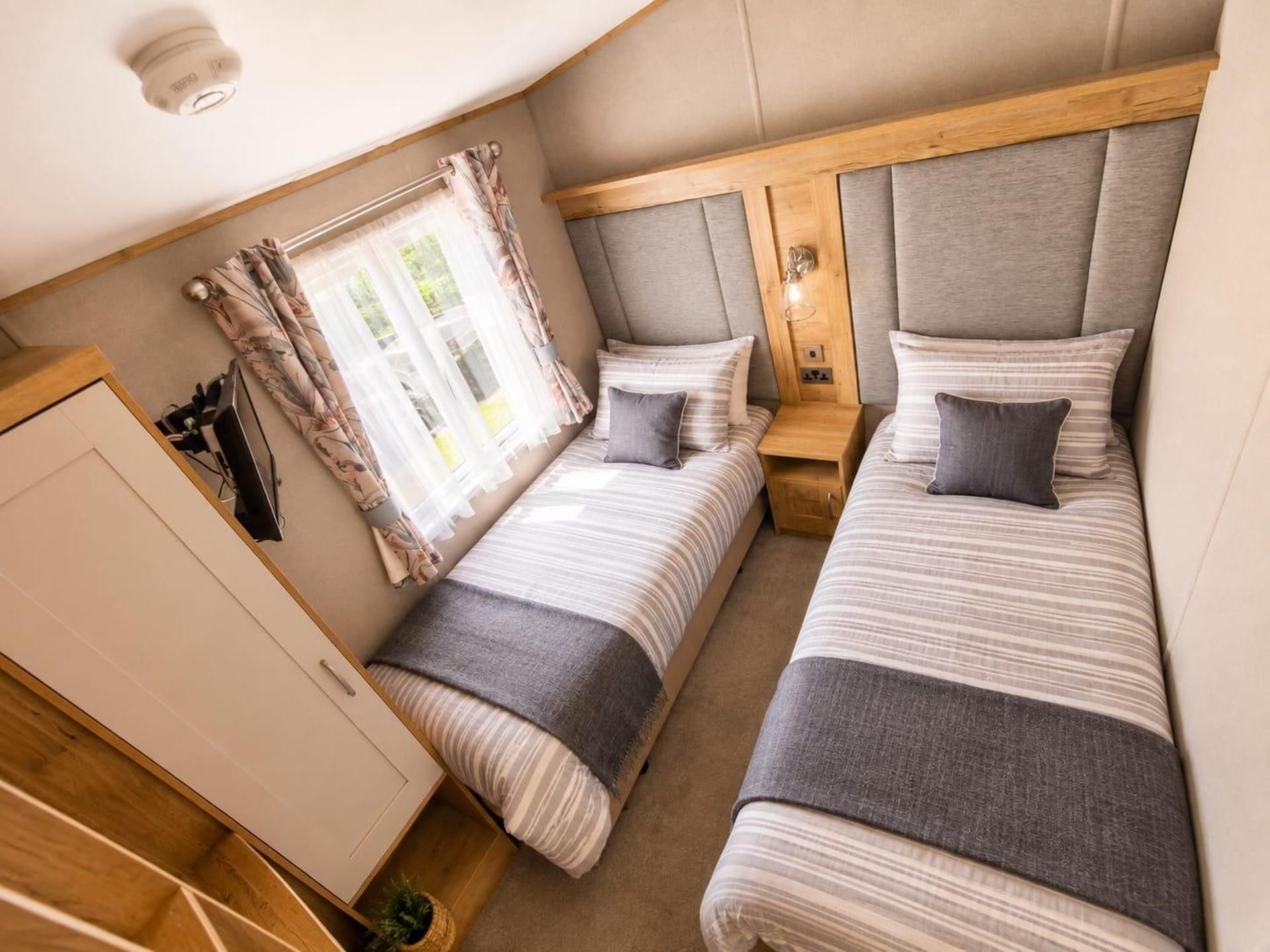 A compact bedroom with two beds, a wardrobe, and a window with curtains.