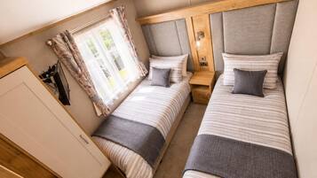 A compact bedroom with two beds, a wardrobe, and a window with curtains.