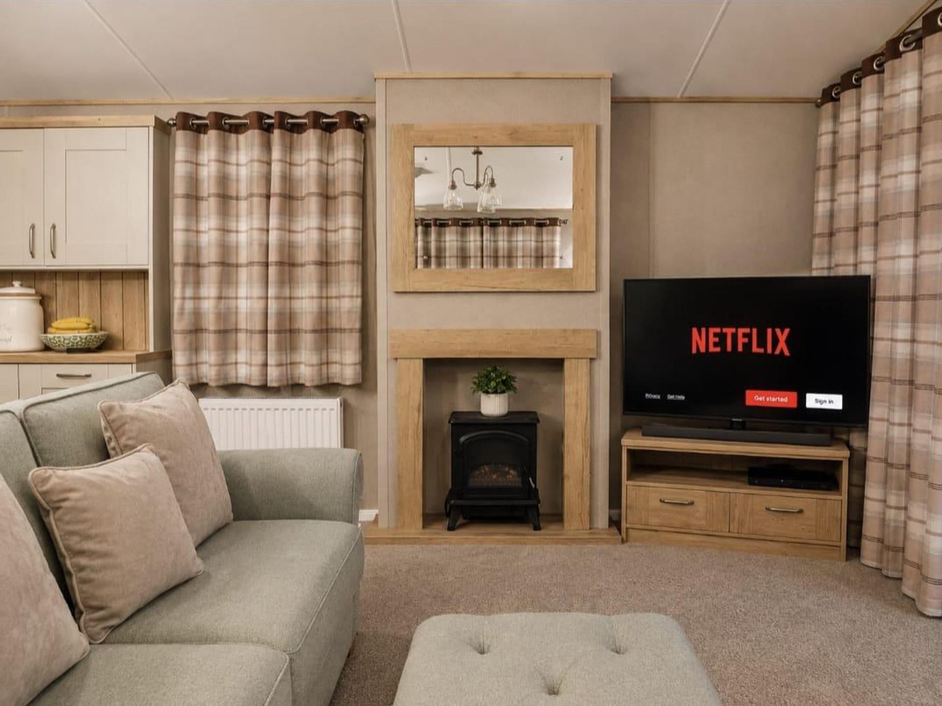 A living room with a sofa, a fireplace, a television, and a kitchen area in the background.