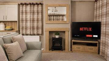 A living room with a sofa, a fireplace, a television, and a kitchen area in the background.